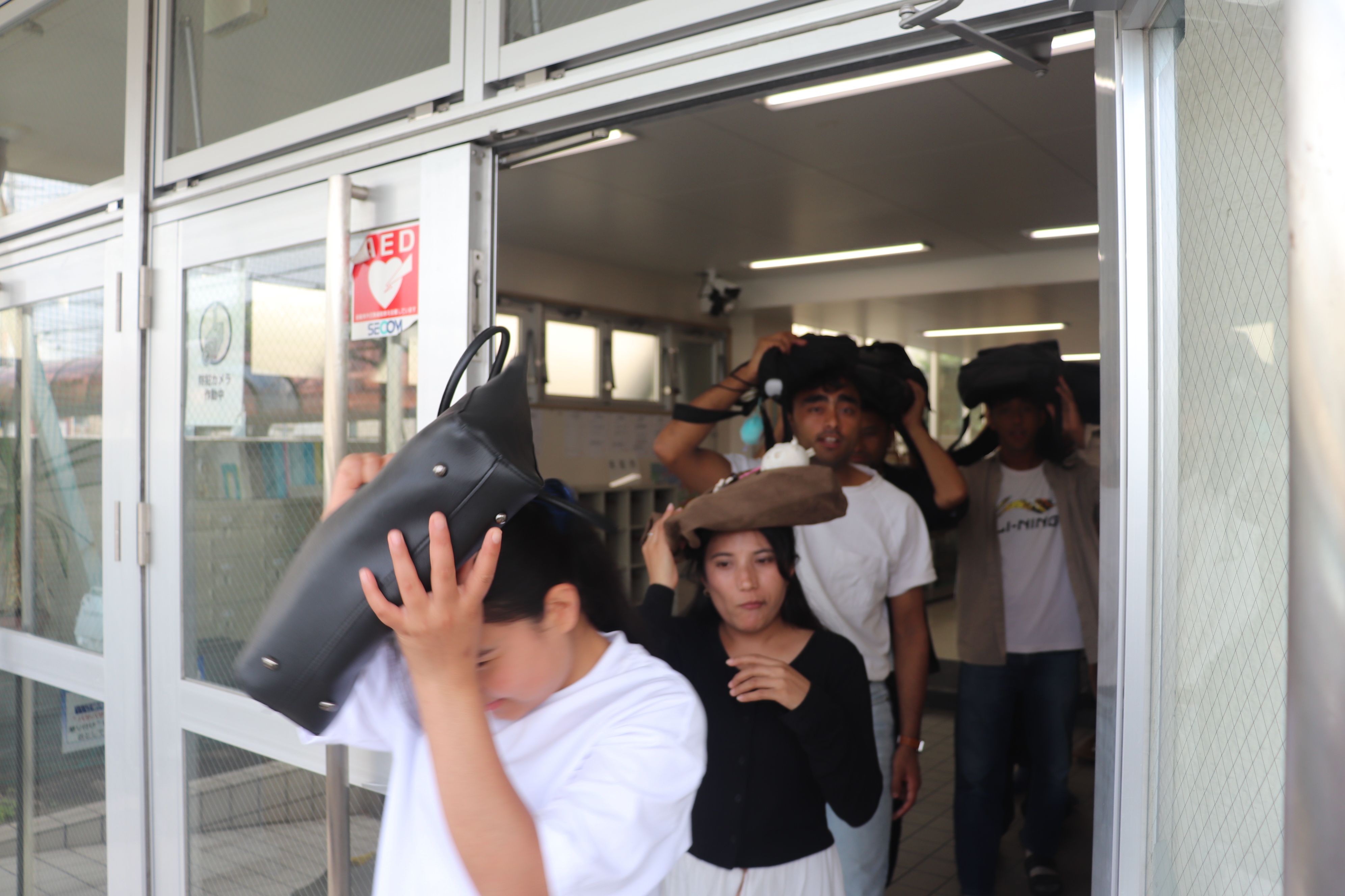 カバンで頭部を隠し避難する学生